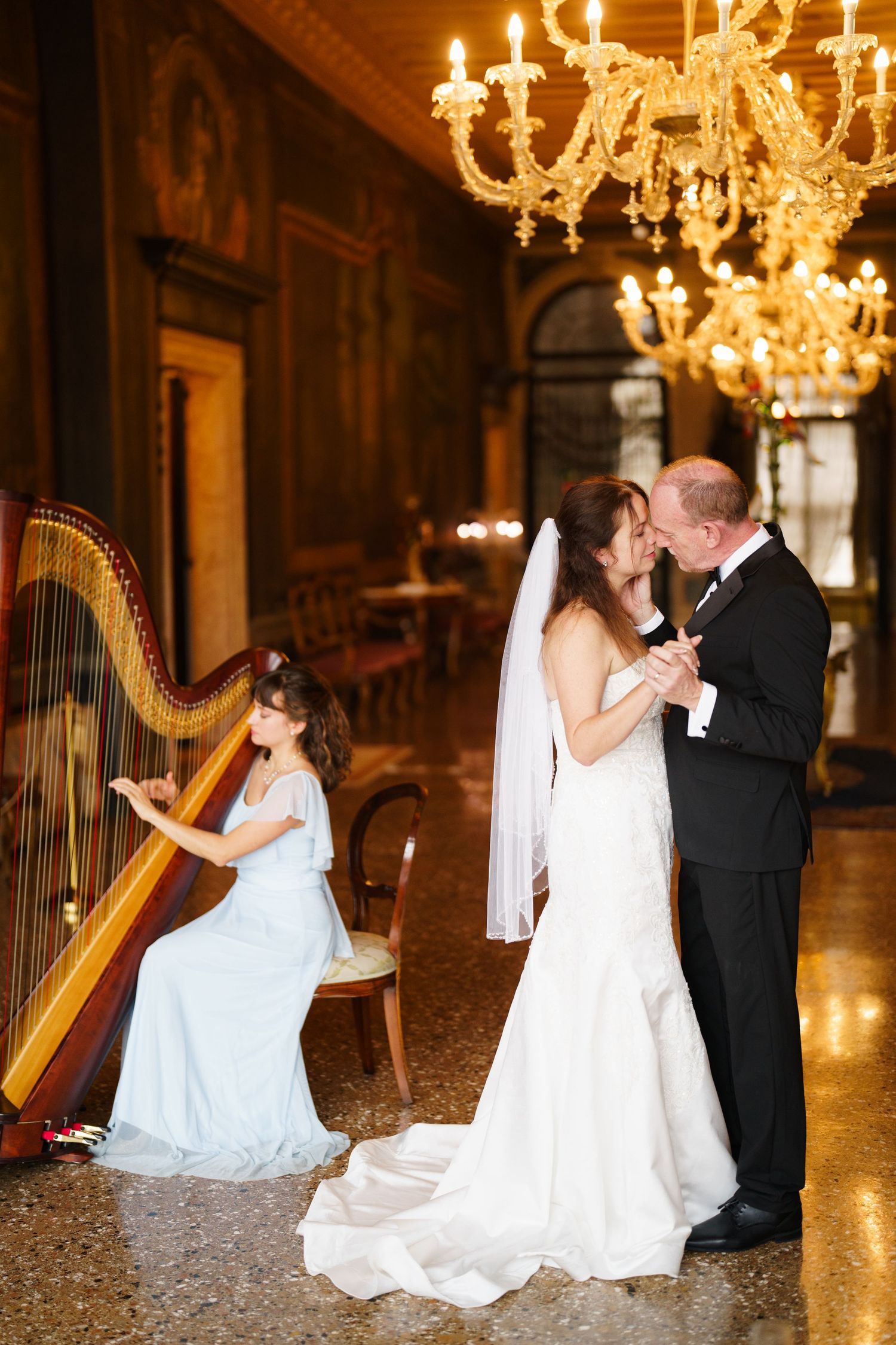 A romantic wedding photo series with a harp in an elegant ballroom with glowing chandeliers.