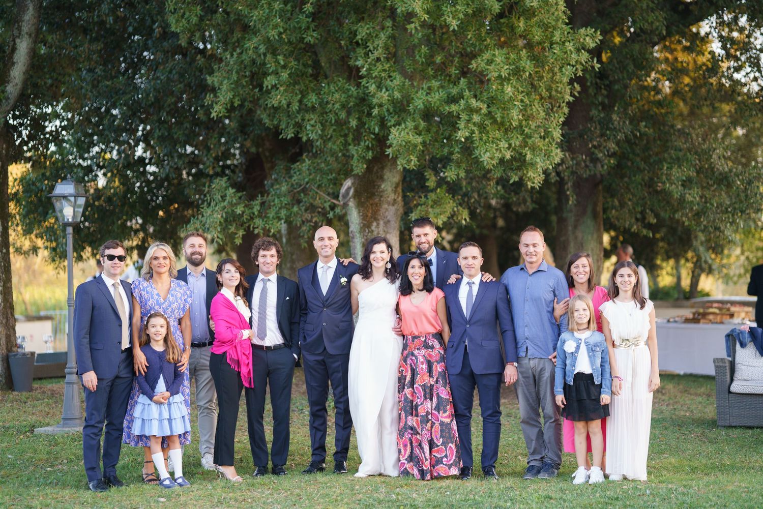 Wedding party and family members pose for formal group photo outdoors.