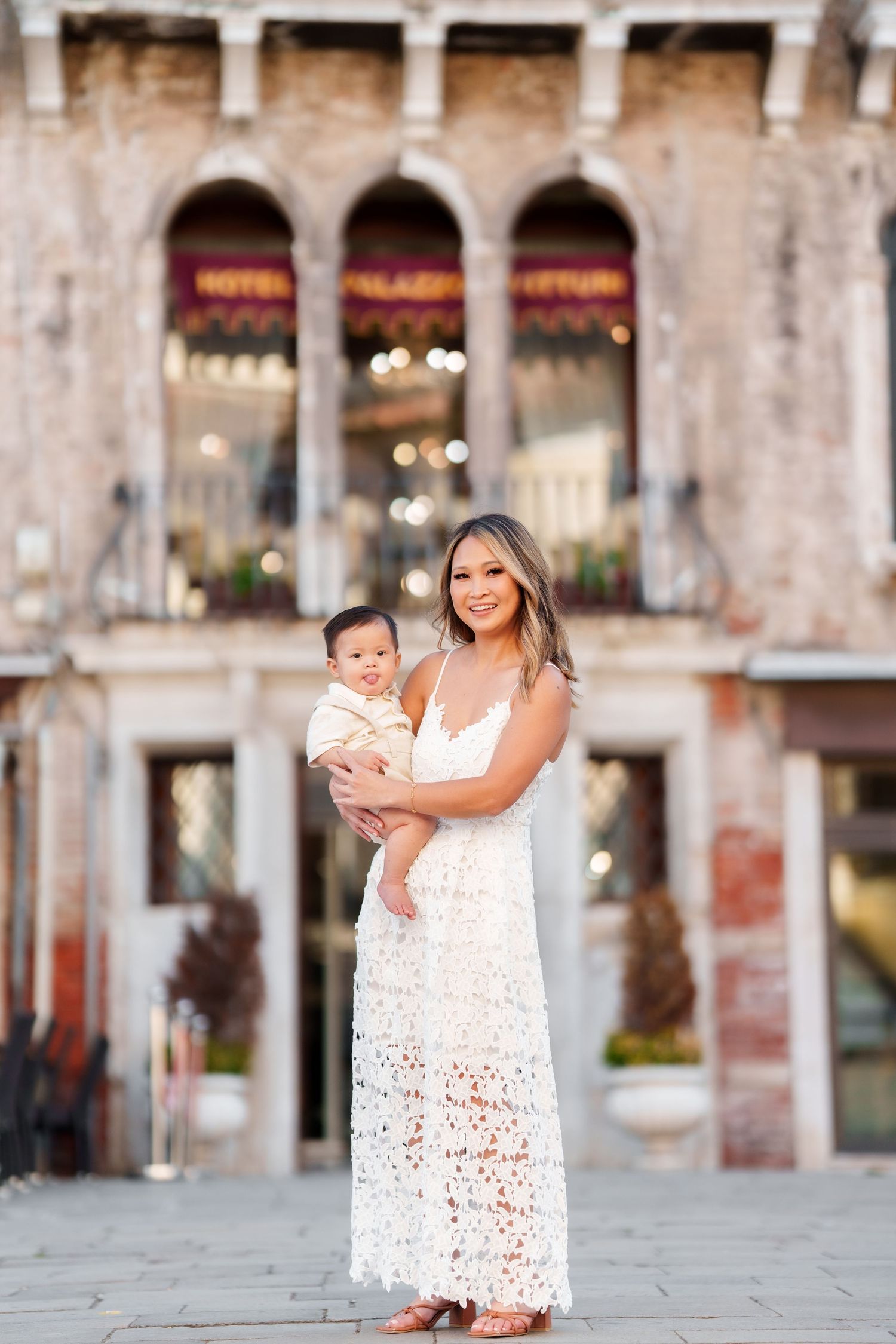 Woman in white lace dress holding baby in front of Hotel Palazzo Vittori in Venice, Italy.