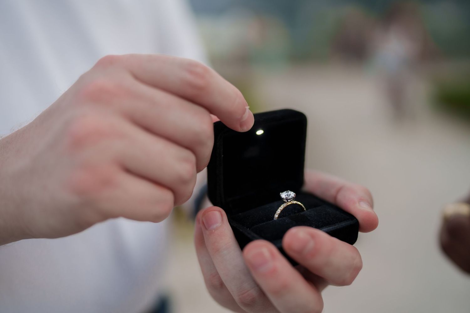 Close-up of hands holding open black velvet box with diamond engagement ring during marriage proposal.
