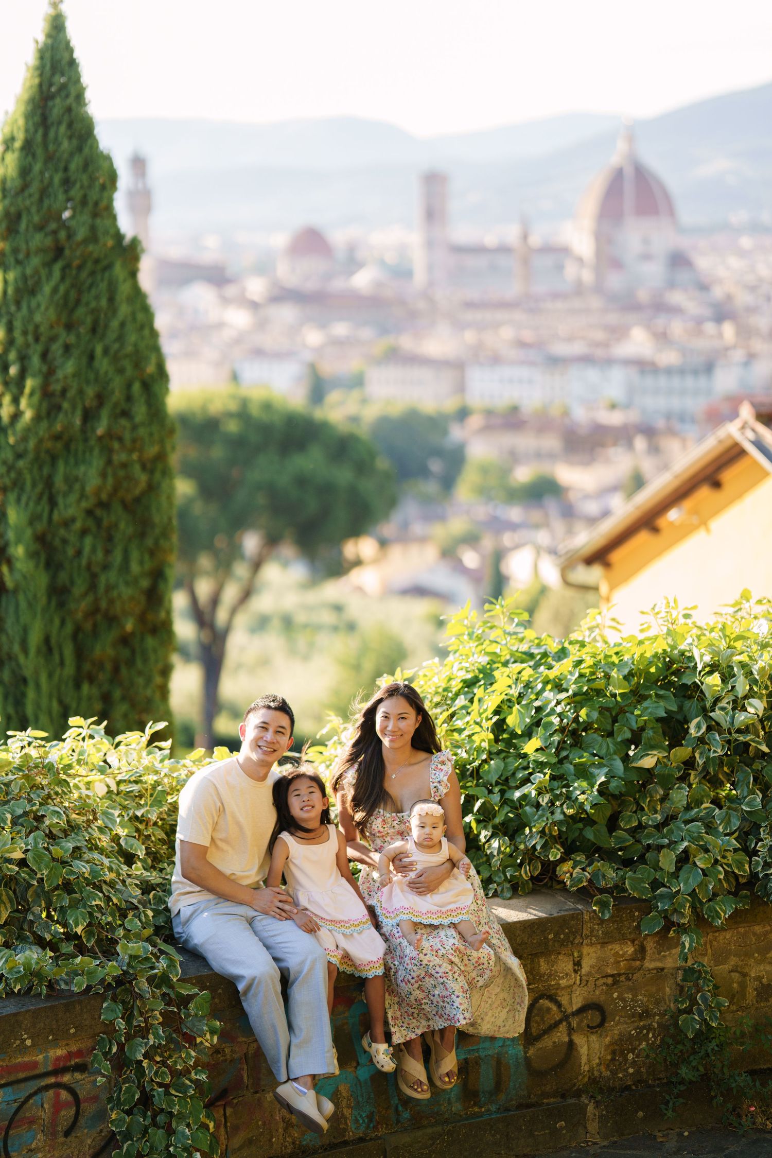 Family of four posing on a stone wall with Florence skyline and Cathedral dome in background, Italy.