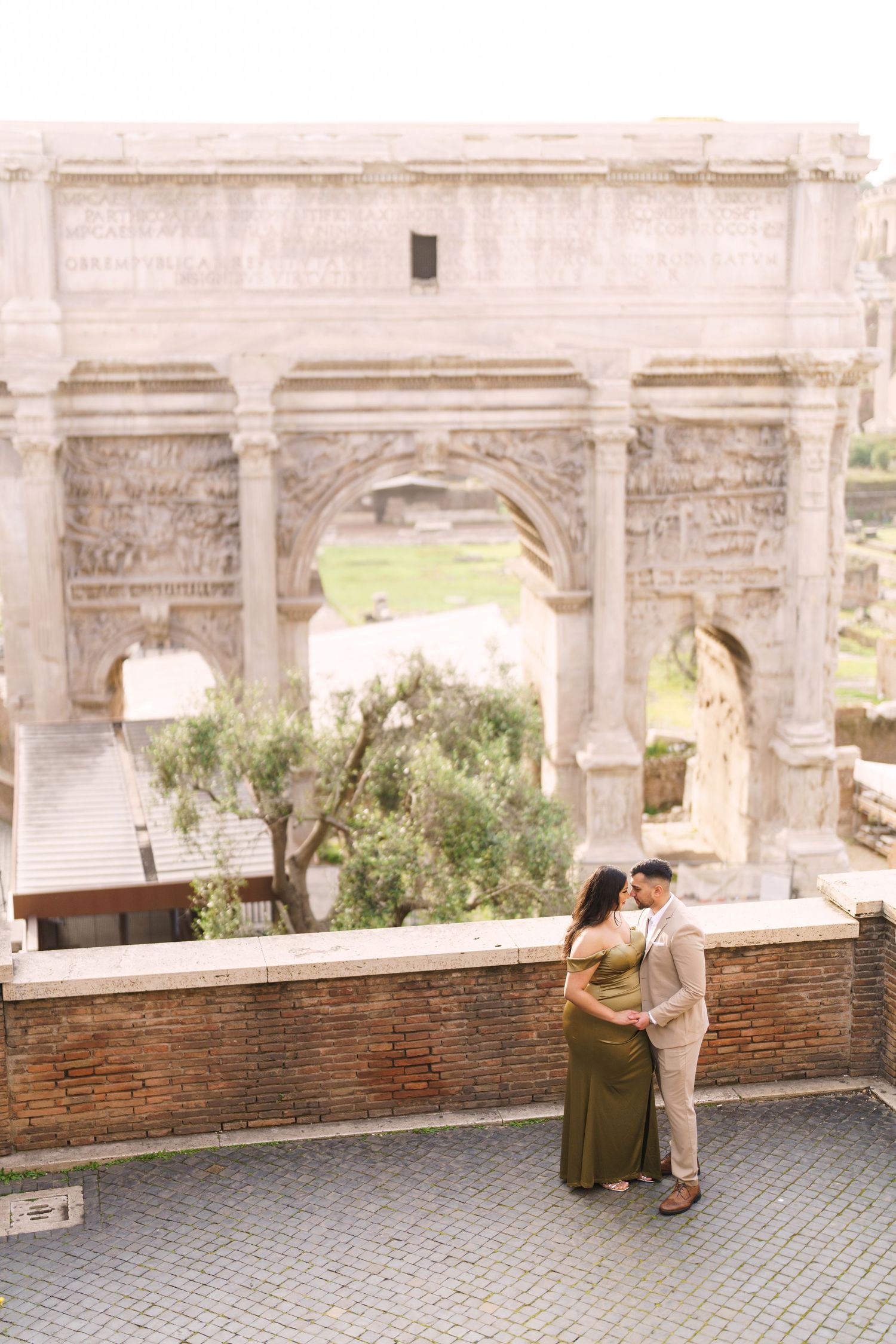 Couple embracing in front of the Arch of Titus in Rome, Italy, with ancient ruins in the background.
