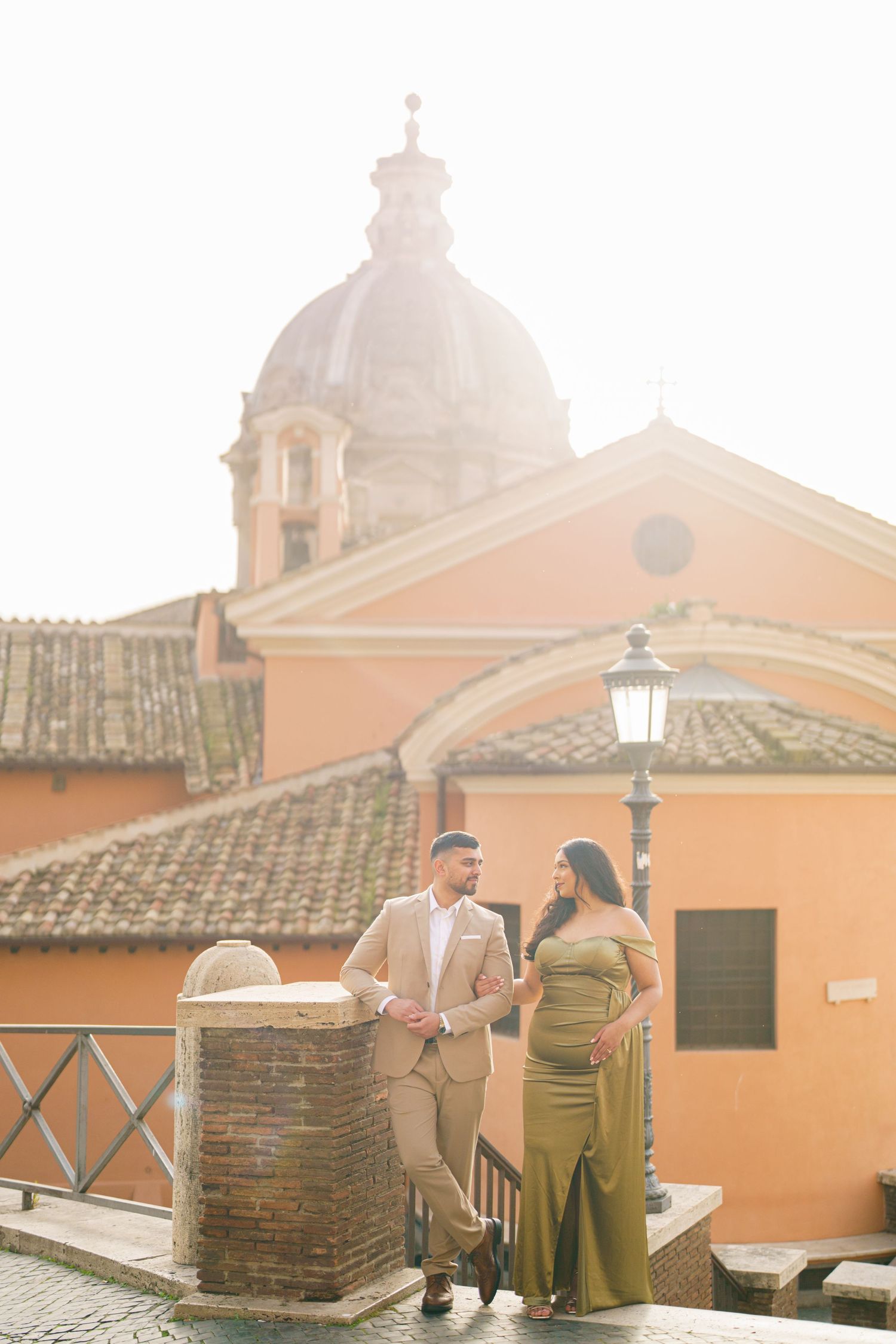Couple posing in front of a Roman church dome and terracotta rooftops in golden sunlight, Rome, Italy.