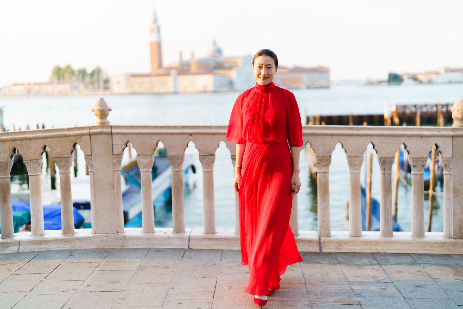 Woman in red dress posing on Venice waterfront terrace with San Giorgio Maggiore island in background.