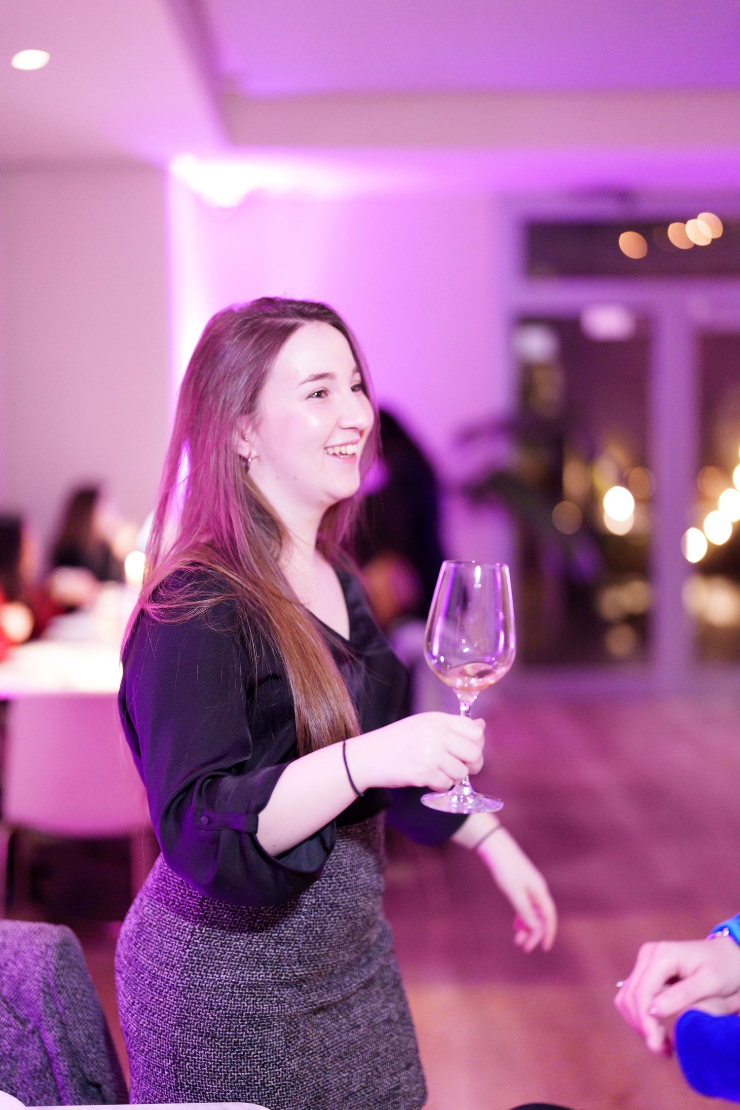 Smiling young woman holding a wine glass at an elegant event with purple ambient lighting.