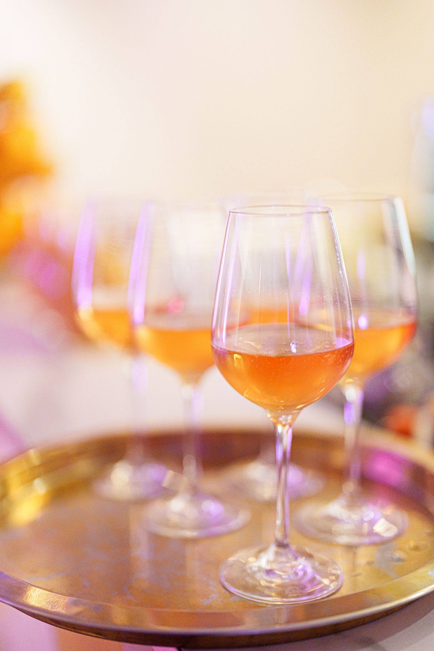 Rose wine glasses on a gold tray at an elegant event, shallow depth of field with warm pink tones.