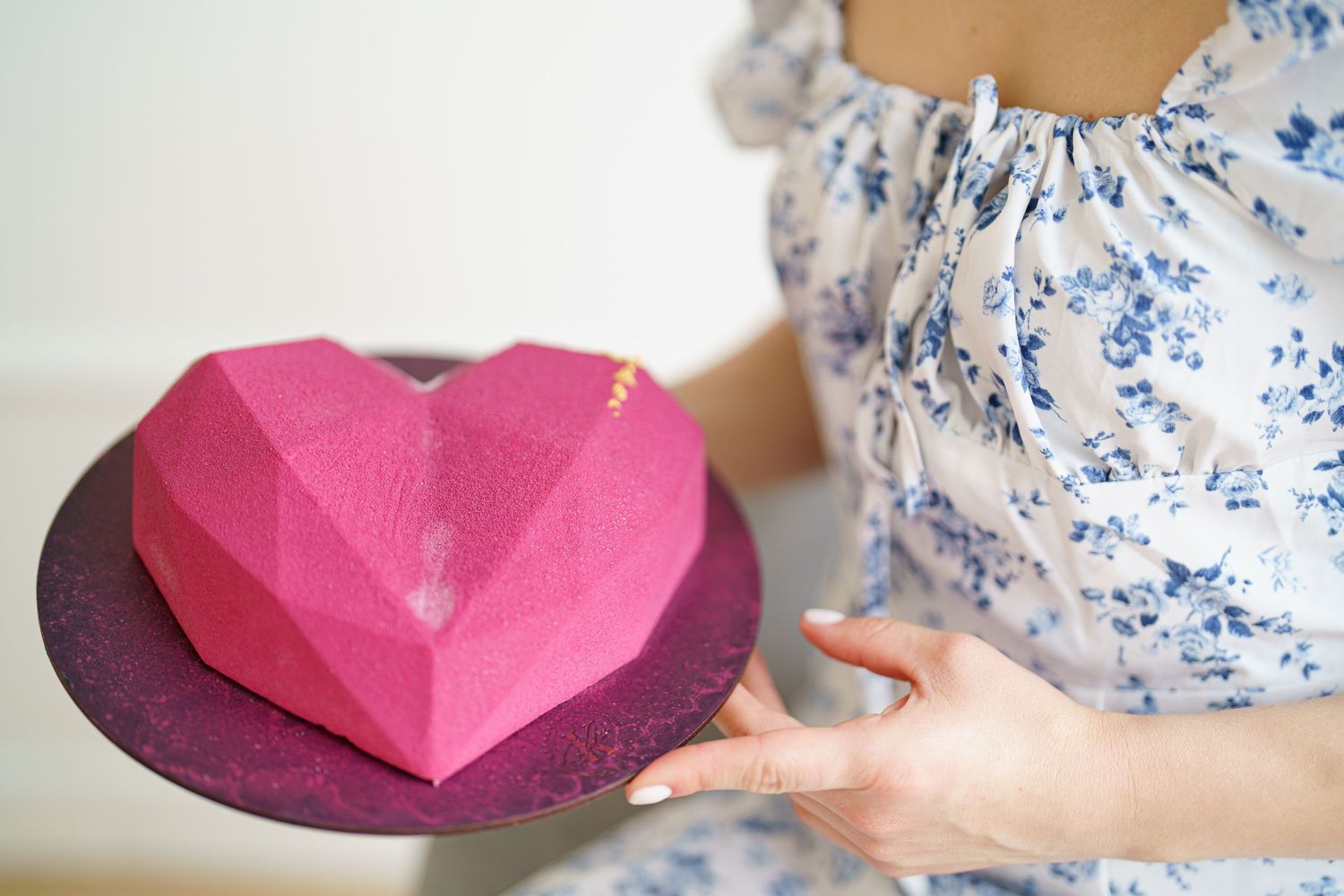 Woman holding a pink geometric heart-shaped cake on a dark plate, perfect for Valentine's Day celebrations.