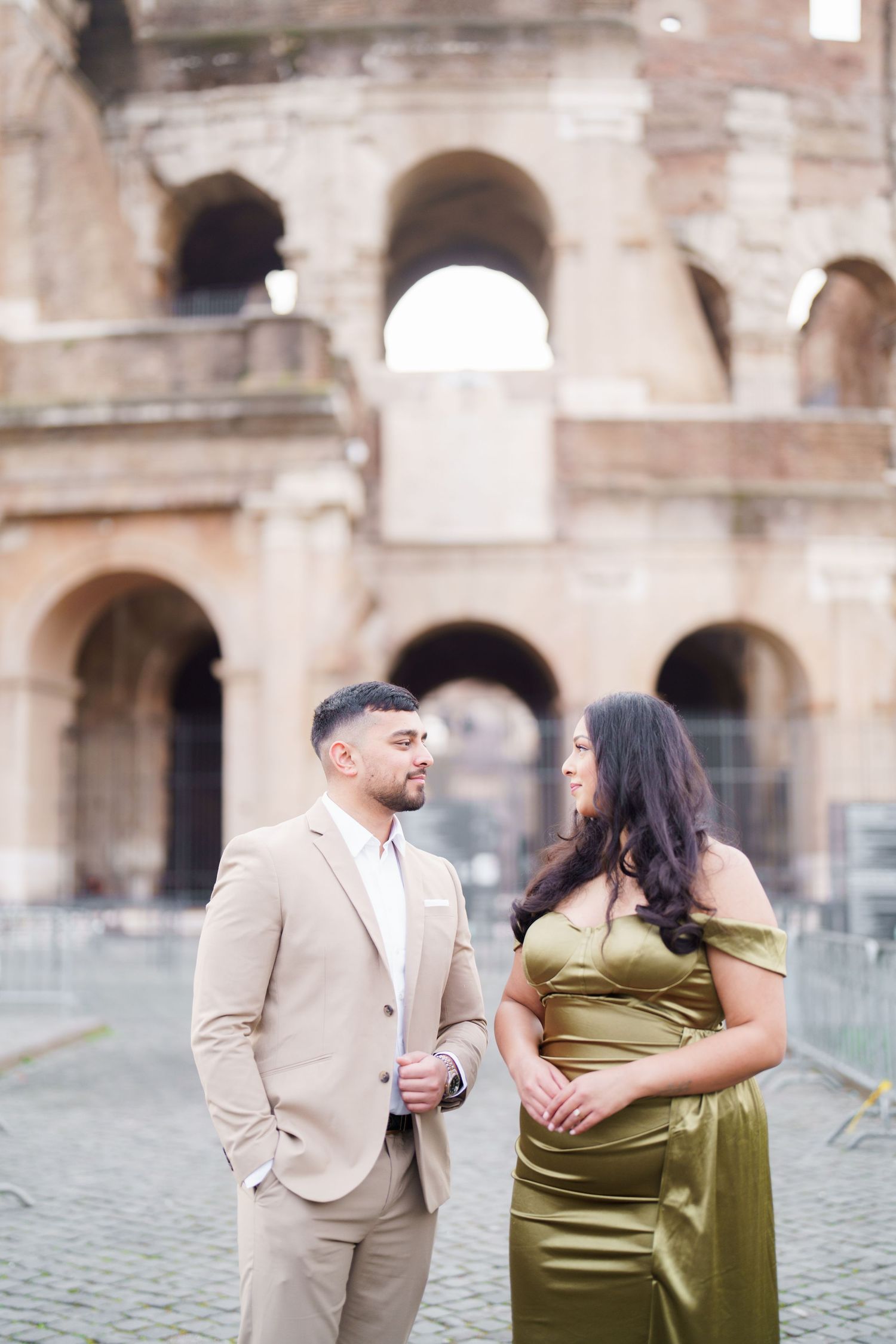 Couple in elegant attire posing romantically in front of the Colosseum in Rome, Italy.