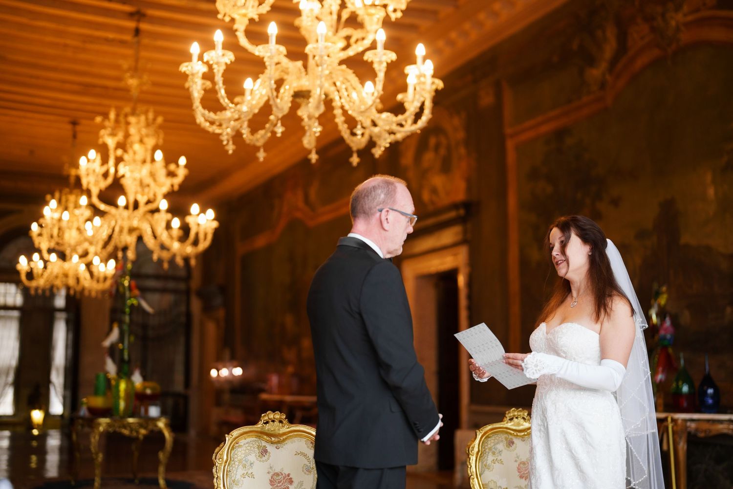 A couple dances under elegant crystal chandeliers in a grand ballroom during a wedding reception.