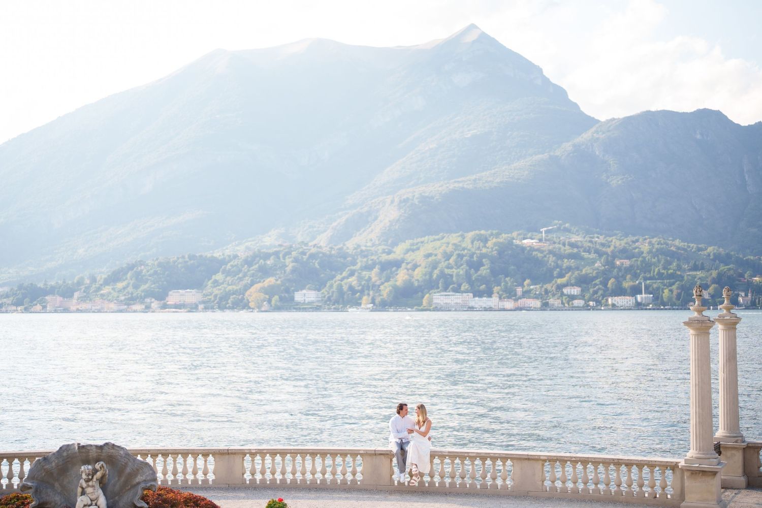 Scenic view of Lake Como with mountains, stone balustrade, and waterfront promenade in Italy.