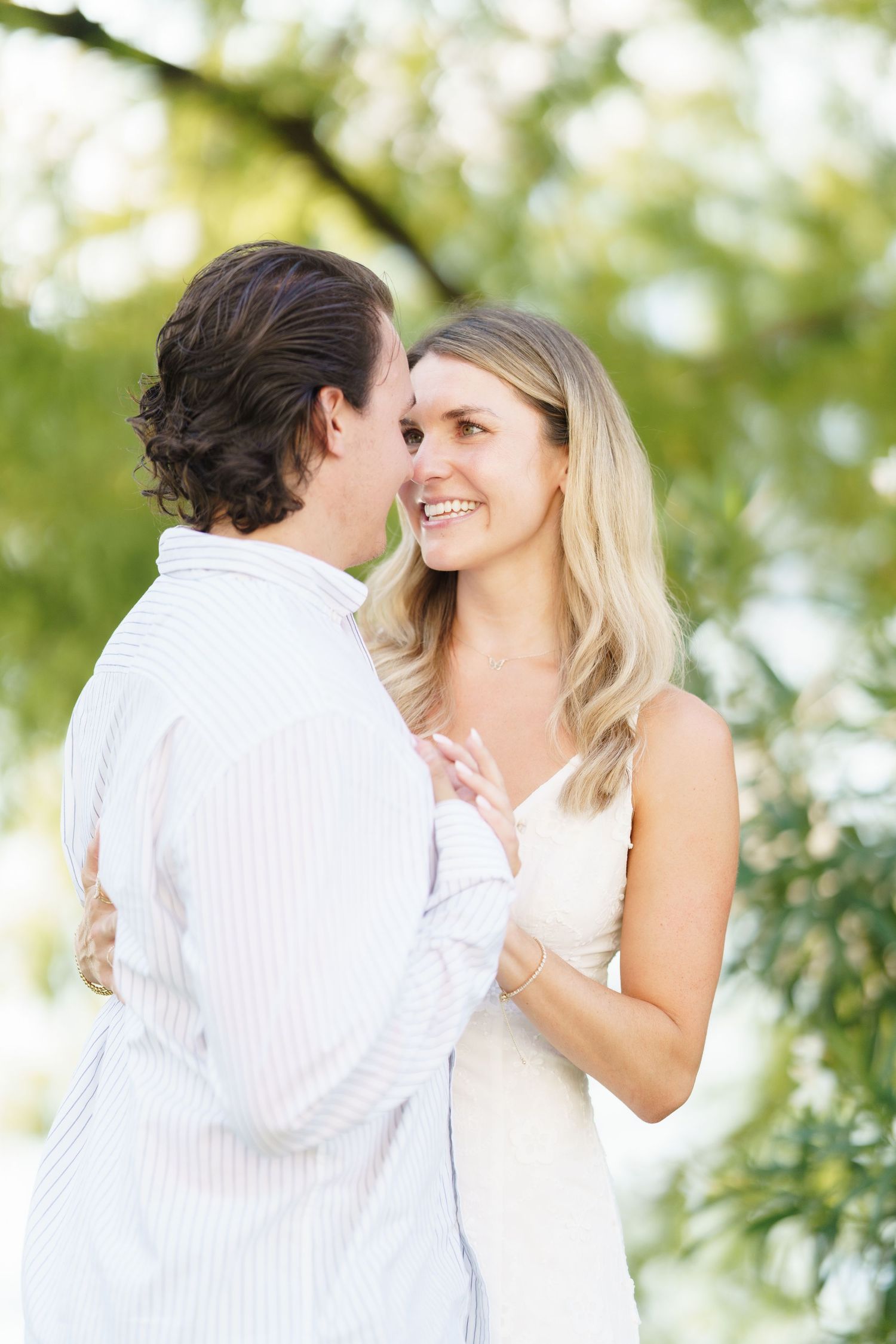 A romantic outdoor moment between a couple in white clothing with soft natural lighting and greenery in the background.