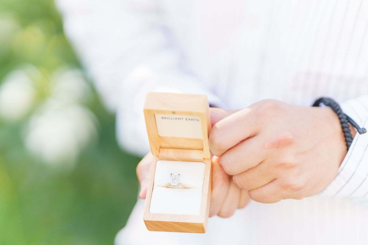 A person in white holds small orange gift boxes against a soft green blurred background.