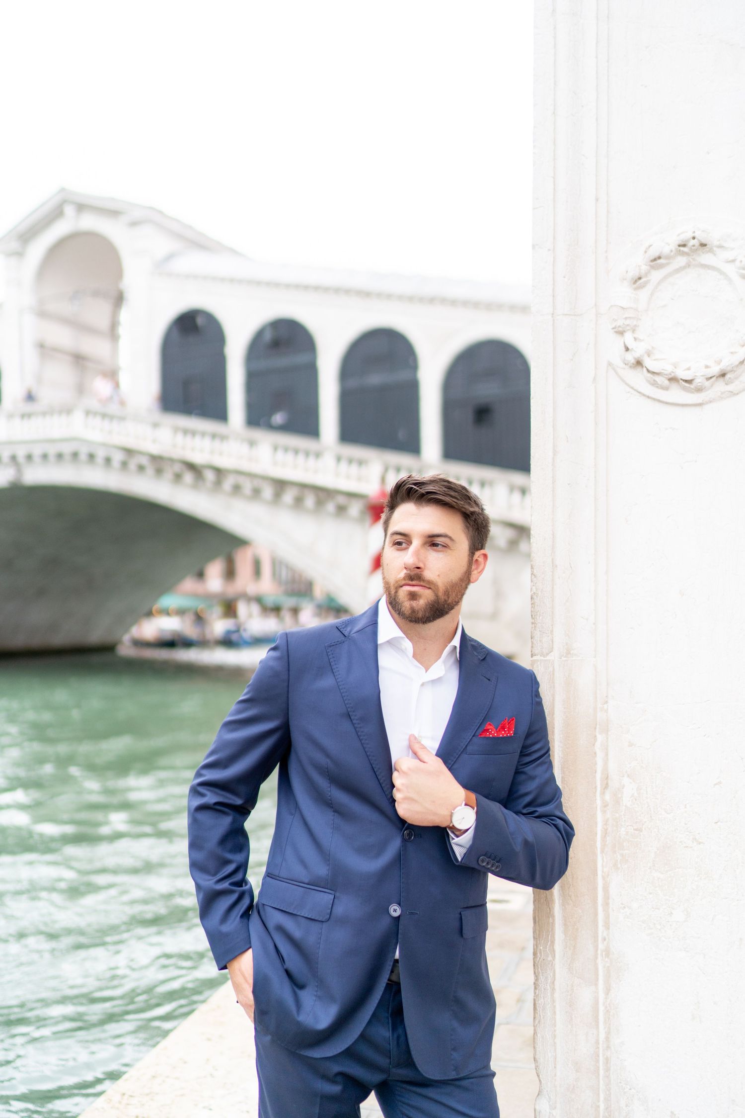 A person in a navy suit poses near the Rialto Bridge and canals of Venice, Italy.