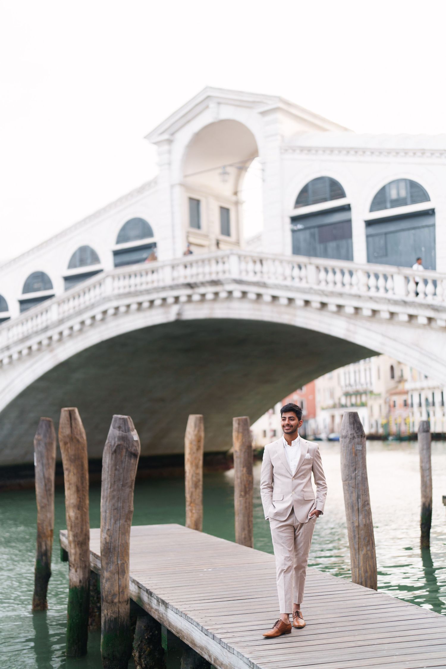 Scenic view of the iconic Rialto Bridge in Venice with wooden dock posts in the foreground along the Grand Canal.