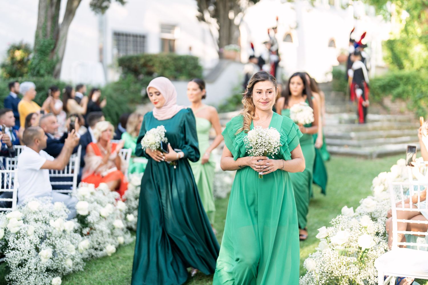 Wedding party members in emerald green dresses gathered at an outdoor ceremony.