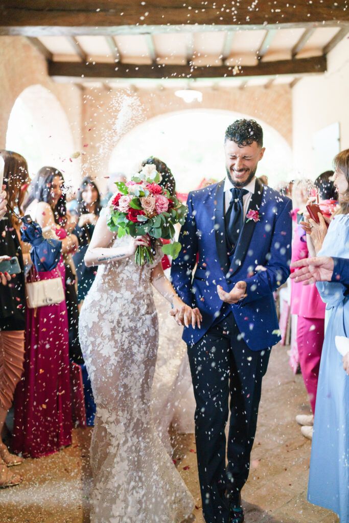 Confetti falls as wedding couple walks through crowd of celebrating guests.