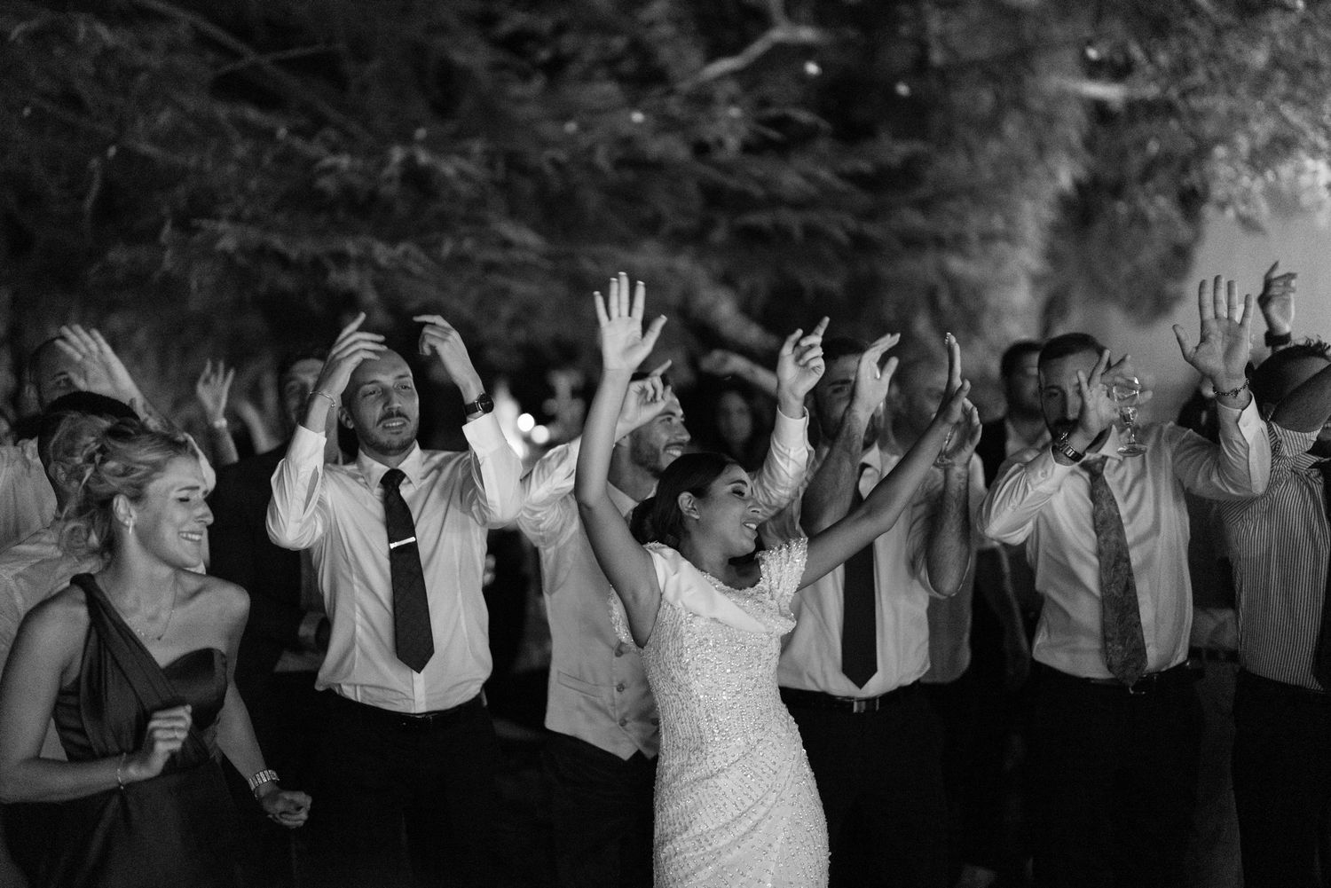 Wedding guests with raised hands celebrating during an outdoor evening reception.