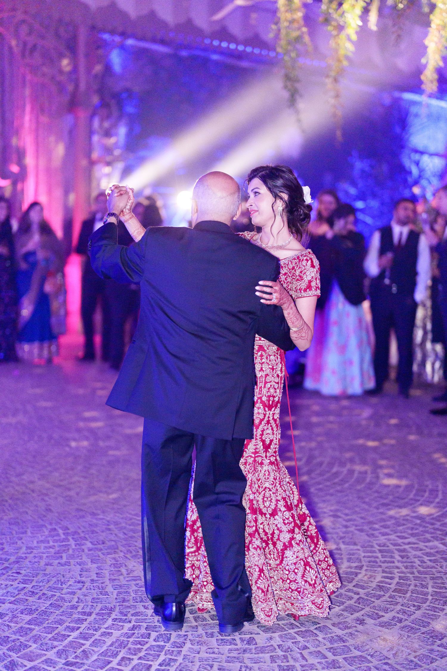 Couples dancing at an elegant reception with dramatic purple lighting and cobblestone flooring.