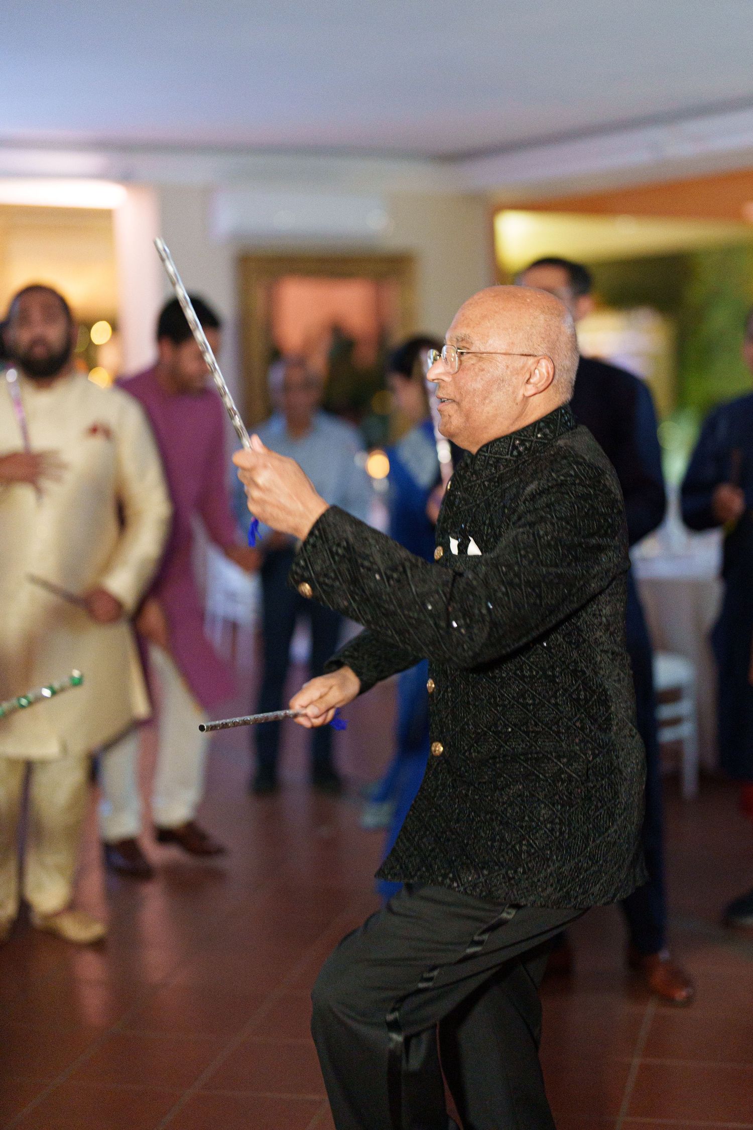 Senior guest in black attire dancing enthusiastically with sparklers at an indoor celebration.