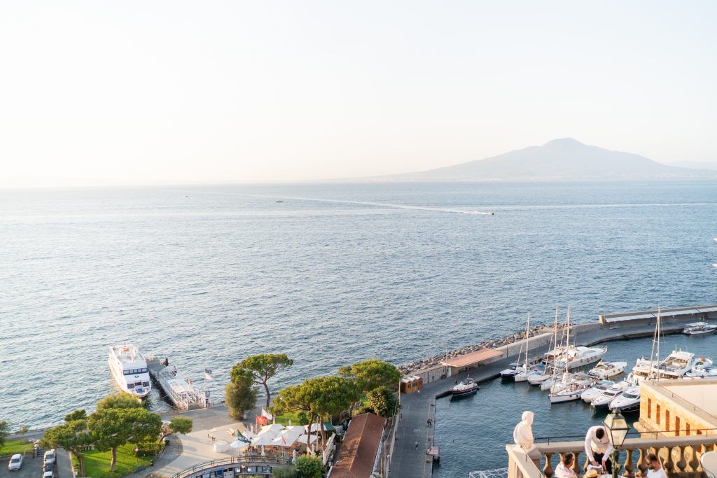 Panoramic view of coastal marina with boats and mountains in background.