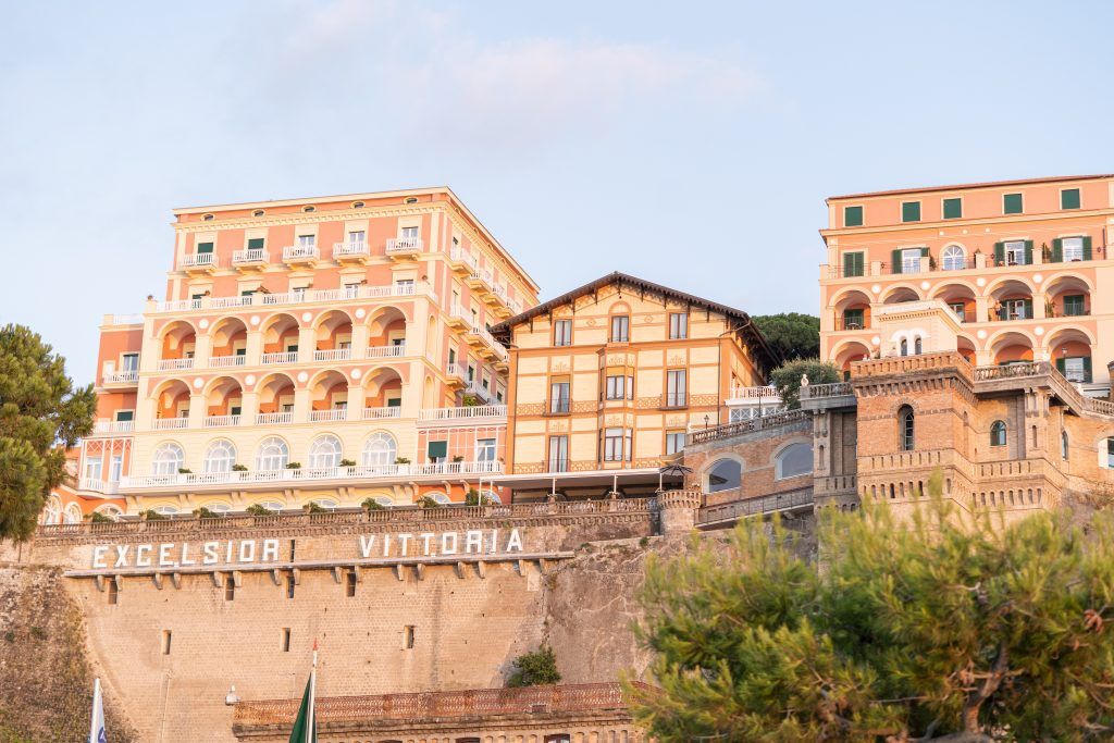 Historic Italian villa with terracotta walls and arched windows built into coastal cliffs.