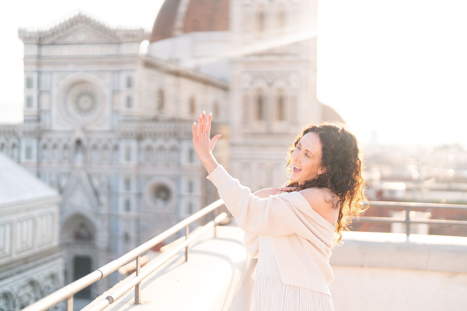 Woman in white dress poses joyfully in front of Florence Cathedral during golden hour sunset in Italy.