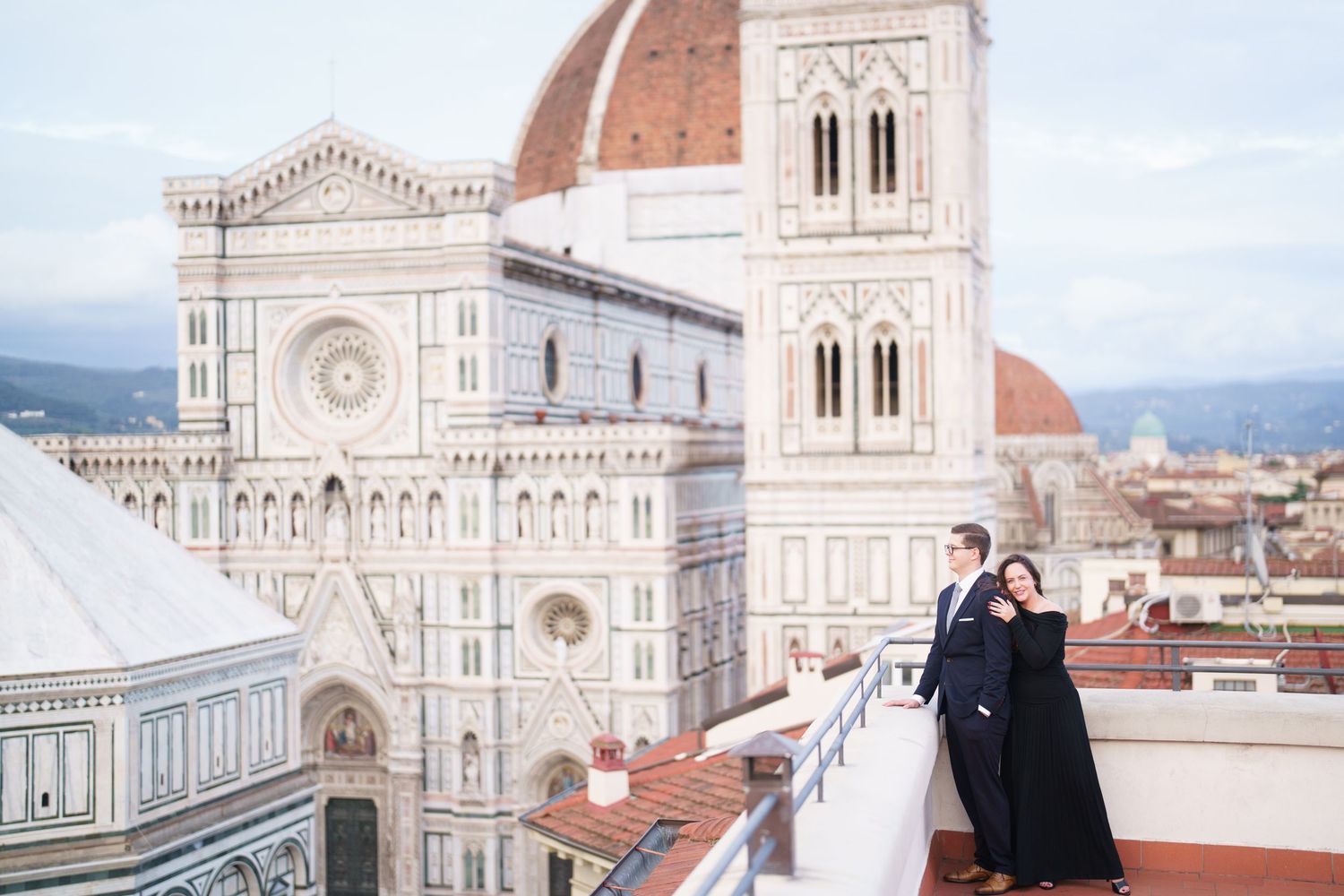 Couple standing on rooftop terrace overlooking Florence Cathedral and Duomo with its iconic Renaissance architecture.