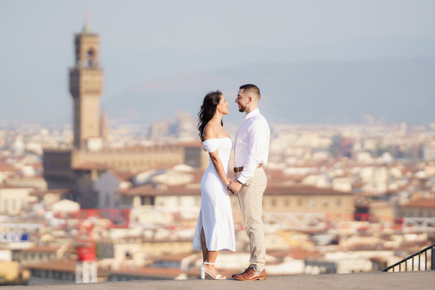 A couple shares a romantic moment overlooking the historic cityscape of Florence, Italy with its iconic Palazzo Vecchio tower.