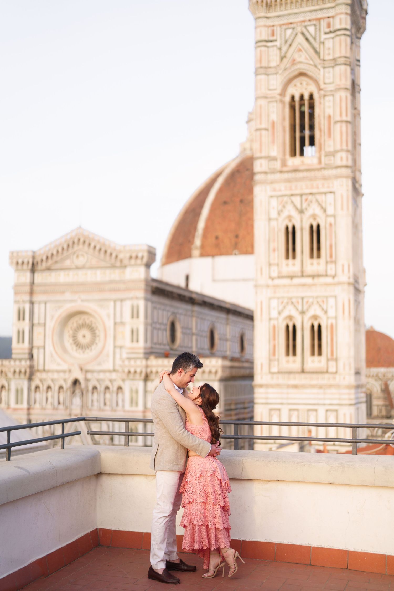 A romantic couple embraces on a rooftop terrace with Florence's Duomo cathedral and Giotto's bell tower in the background.