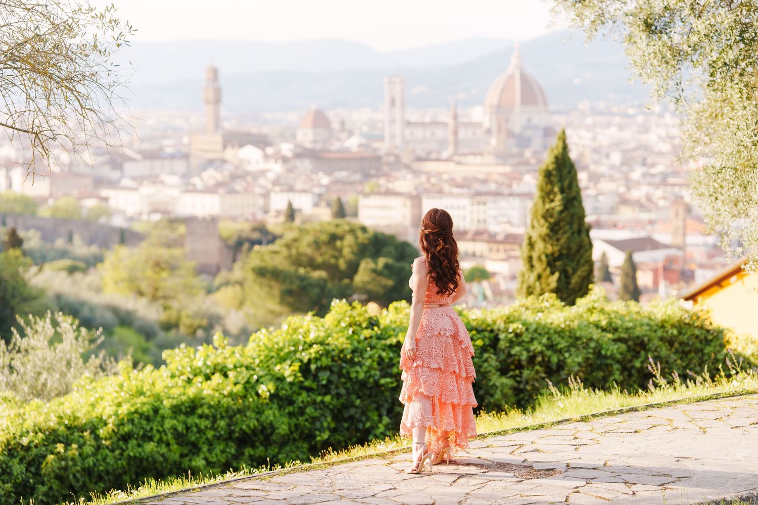 Person in pink dress admires stunning Florence cityscape from hilltop viewpoint on sunny day in Italy.
