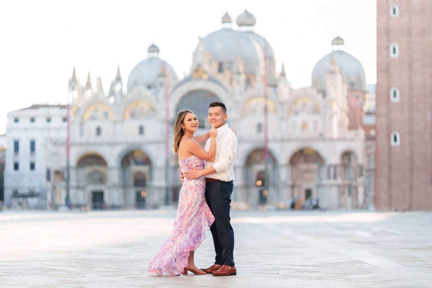 Couple embracing in St. Mark's Square, Venice, with the iconic Basilica di San Marco in the background.