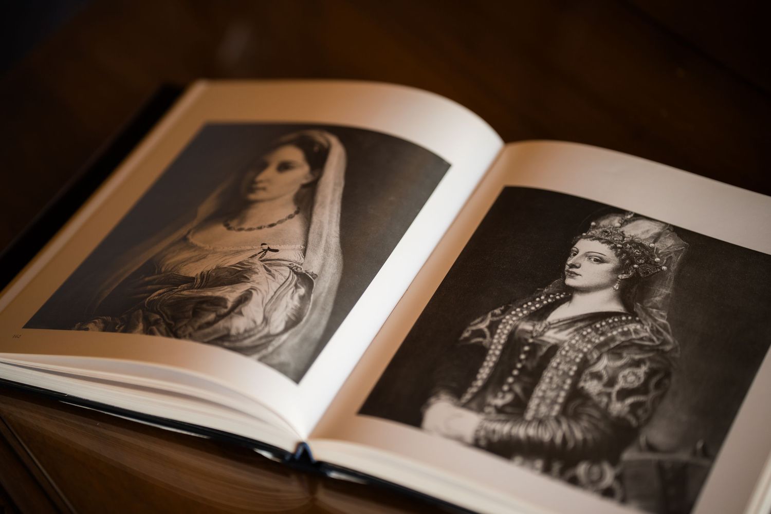 Open book displaying two black and white portrait photographs of elegantly dressed women in ornate costumes on a wooden table.