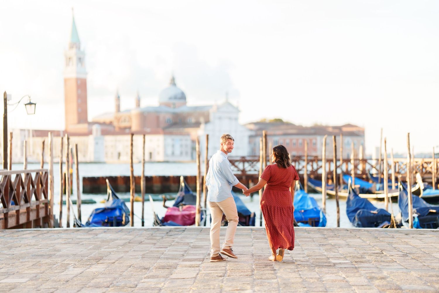 Couple dancing on Venice waterfront with gondolas and San Giorgio Maggiore church in soft morning light.