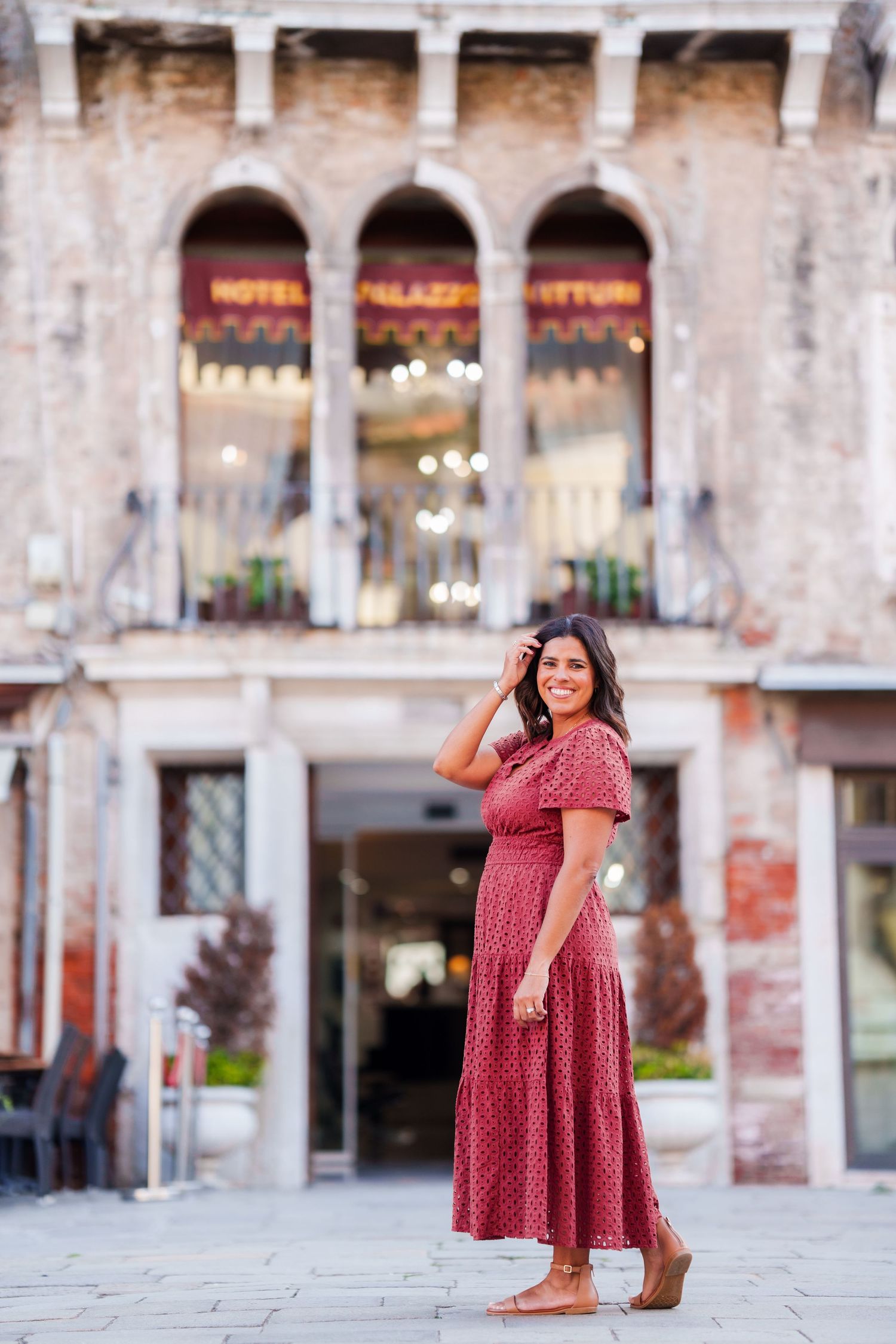 Woman in red maxi dress smiling outside Hotel Palazzo Vitturi in Venice, Italy.