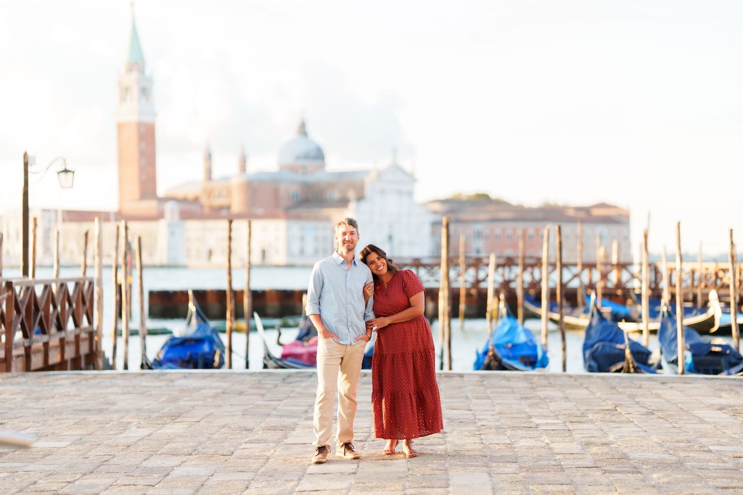 Couple embracing on Venice waterfront with gondolas and San Giorgio Maggiore church in background.