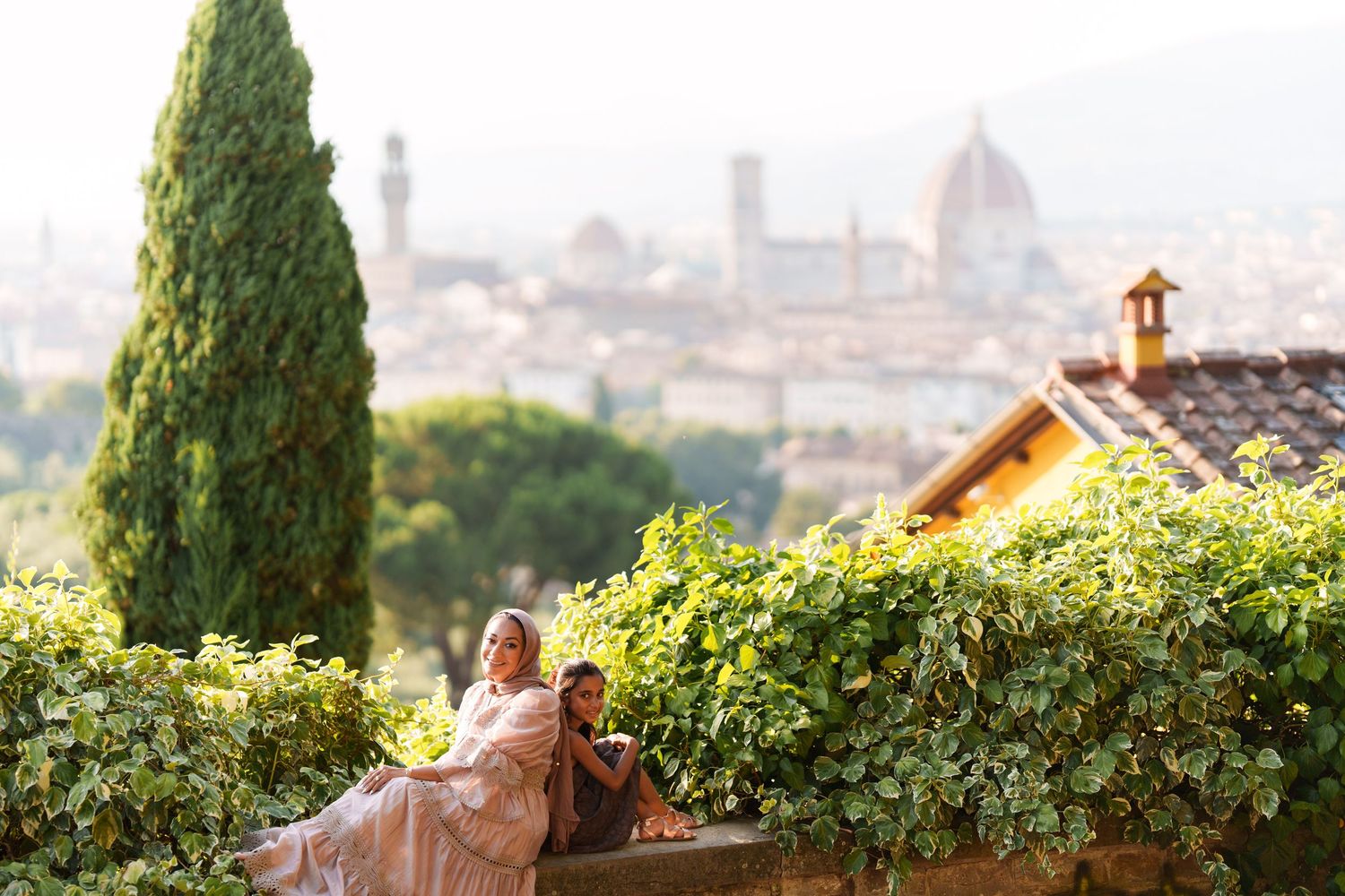 Woman in pink dress sitting among lush greenery with Florence skyline and Duomo cathedral in background.
