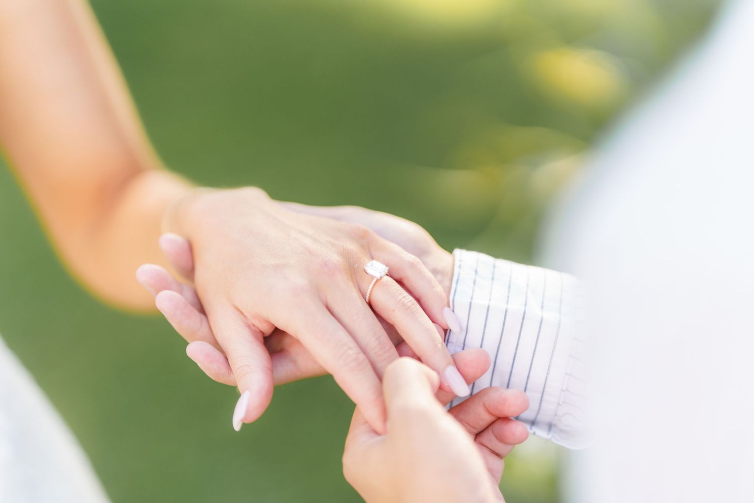 Two people holding hands outdoors share a gentle moment in a natural setting with soft sunlight and greenery.