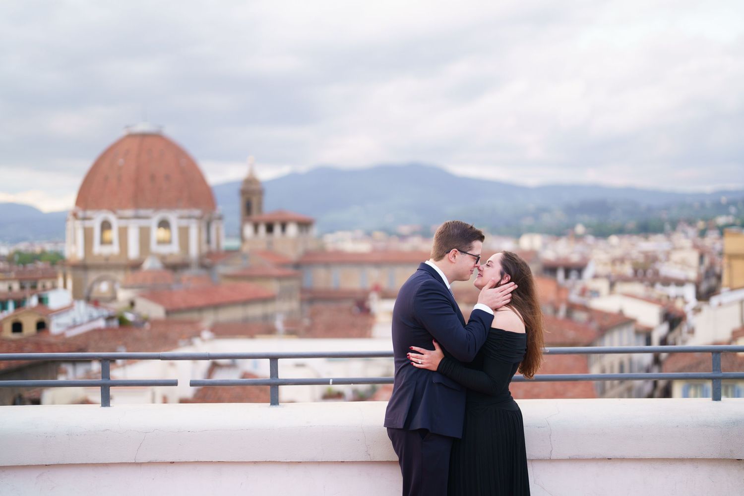Romantic couple shares tender moments on a rooftop terrace overlooking a scenic Italian cityscape with domed buildings.