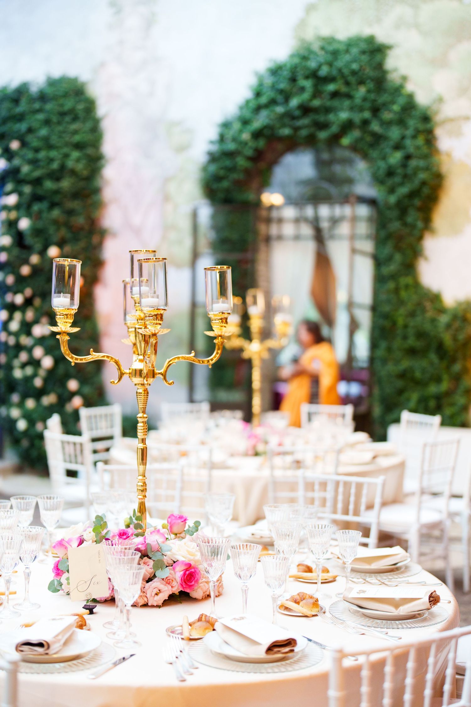 Elegant table settings with gold candelabras and pink roses in a courtyard venue.