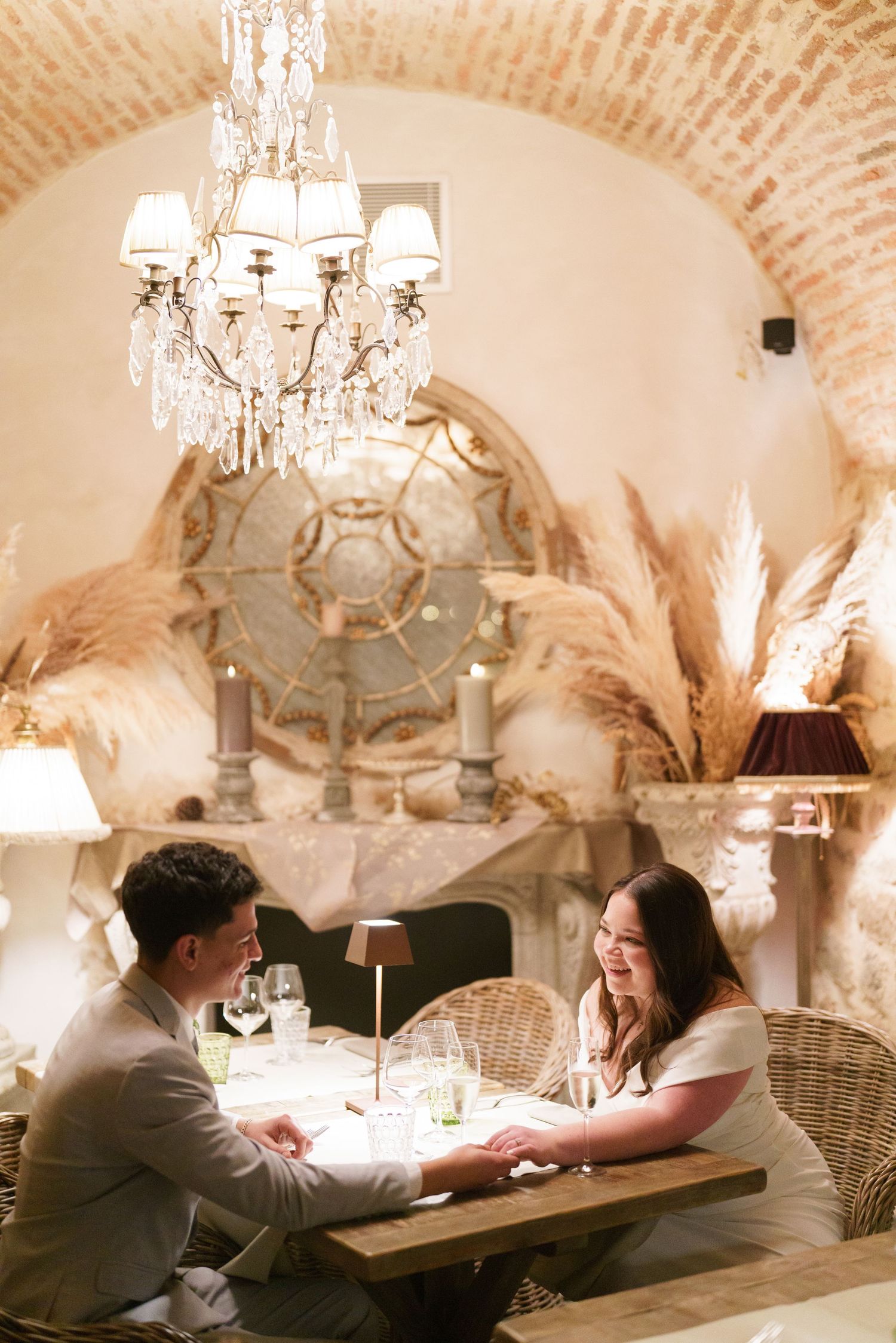 Couples enjoying an intimate dinner setting under arched brick ceilings with crystal chandeliers.