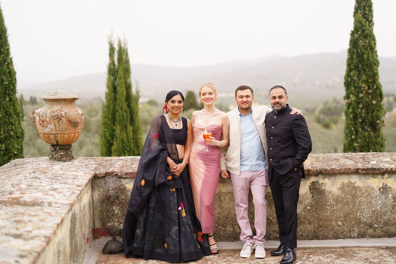Group photo on stone terrace with cypress trees and mountains creating scenic backdrop.