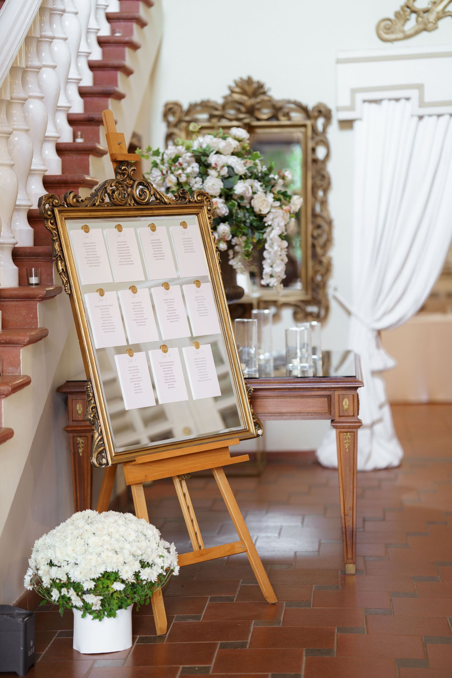 Elegant gold-framed seating chart display on wooden easels with white floral arrangements.