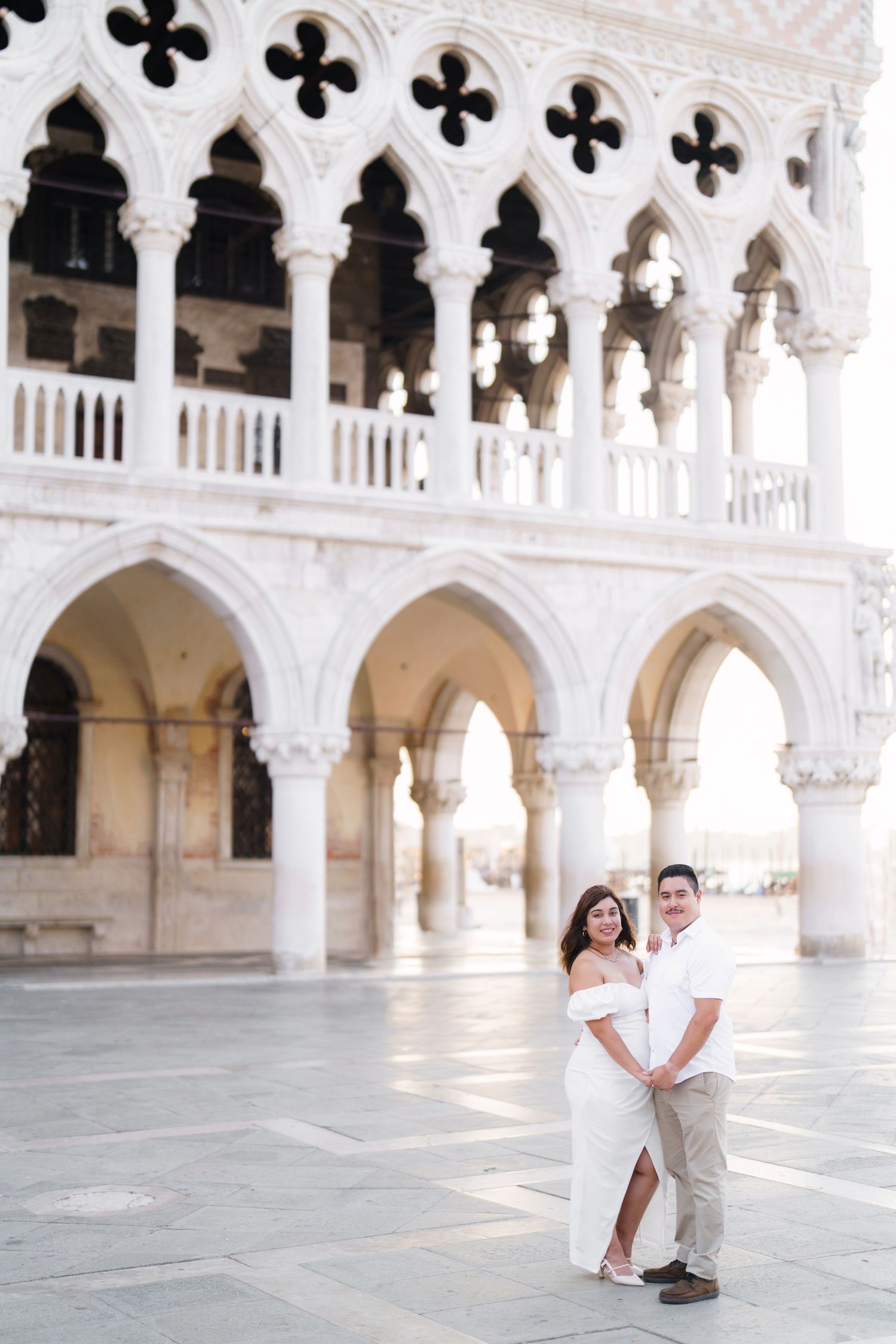 Couple poses in romantic photoshoot under ornate white arches of Venetian Gothic architecture in Venice, Italy.