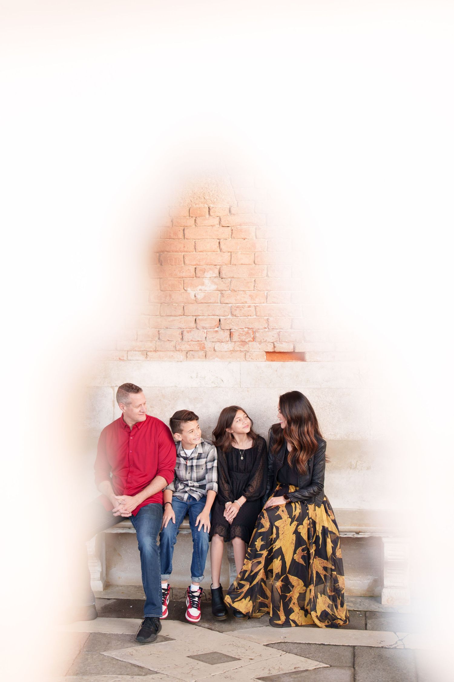 photographer venice A family sits together on white stone steps against a brick wall with a warm vignette effect.