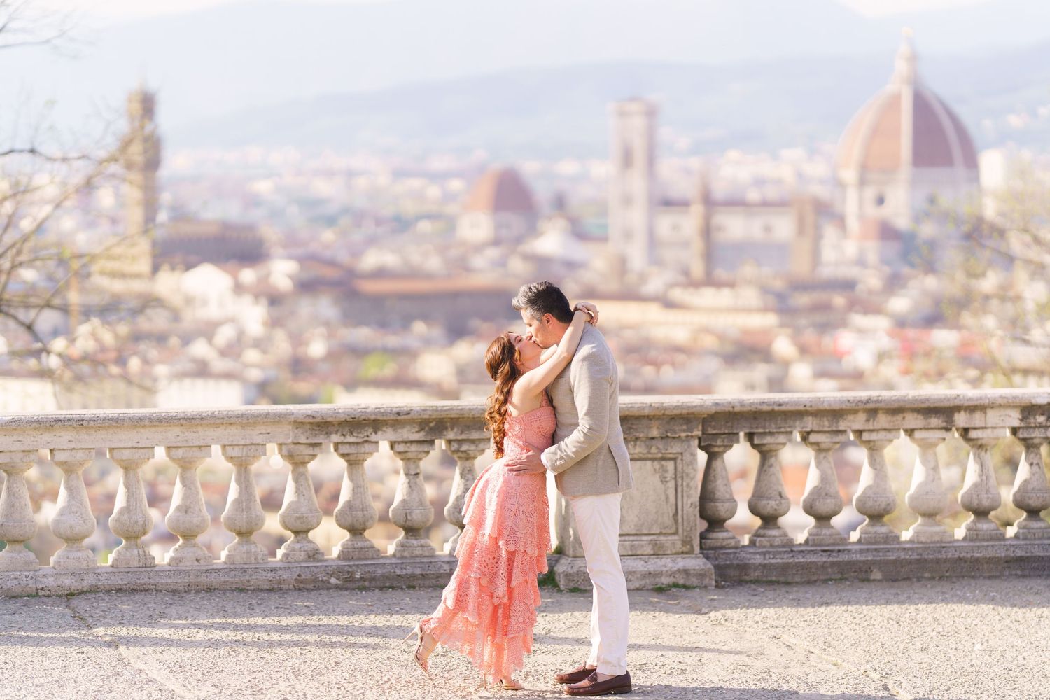A couple embraces on a terrace overlooking Florence, Italy with the iconic Duomo cathedral visible in the background.
