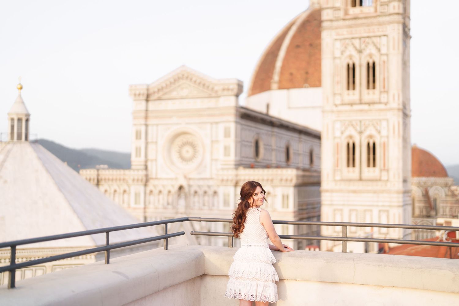 Woman in white dress poses at sunrise on a terrace overlooking the Florence Cathedral in Italy.