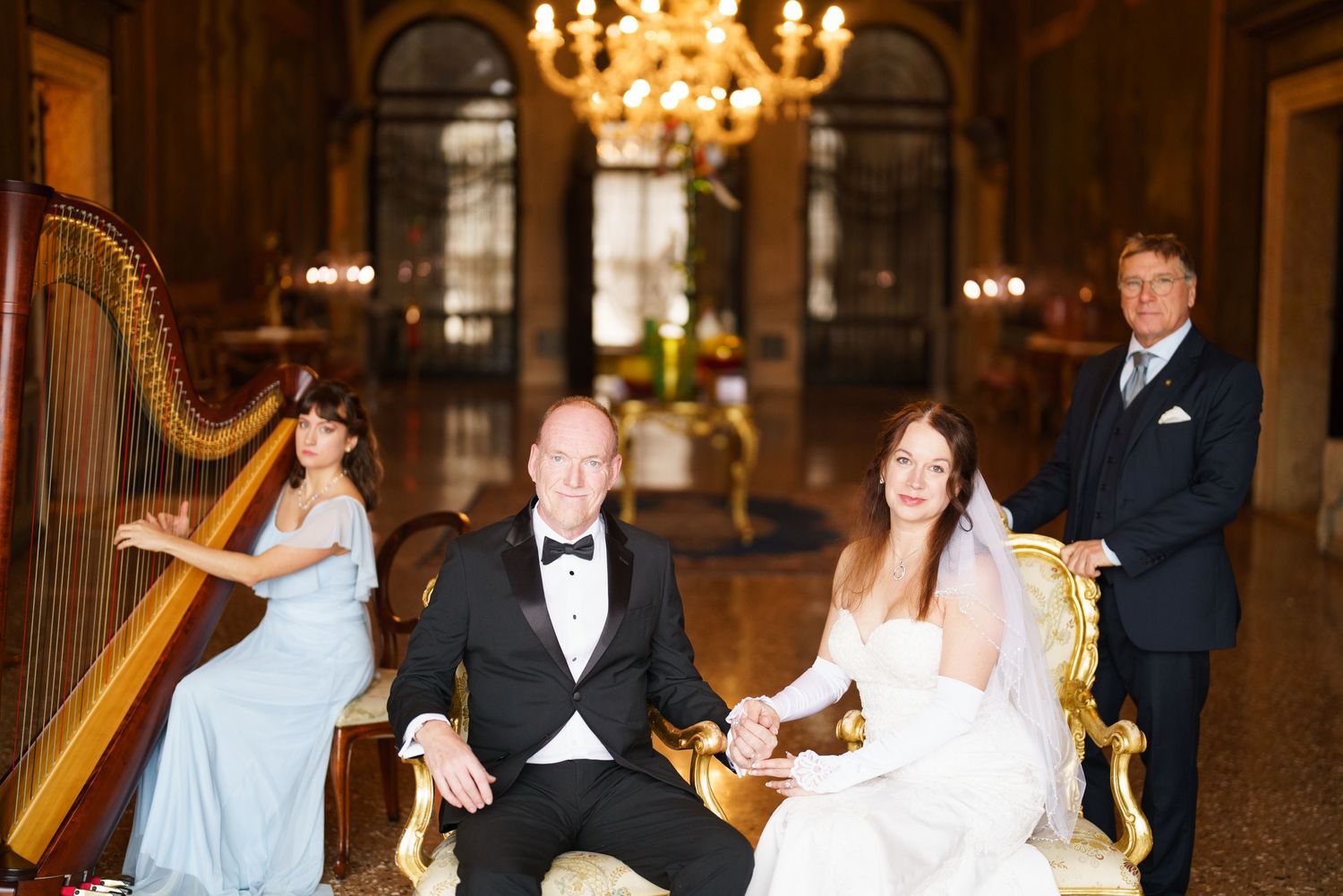 Elegant wedding reception in a grand ballroom with chandeliers and guests dancing on a wooden dance floor.