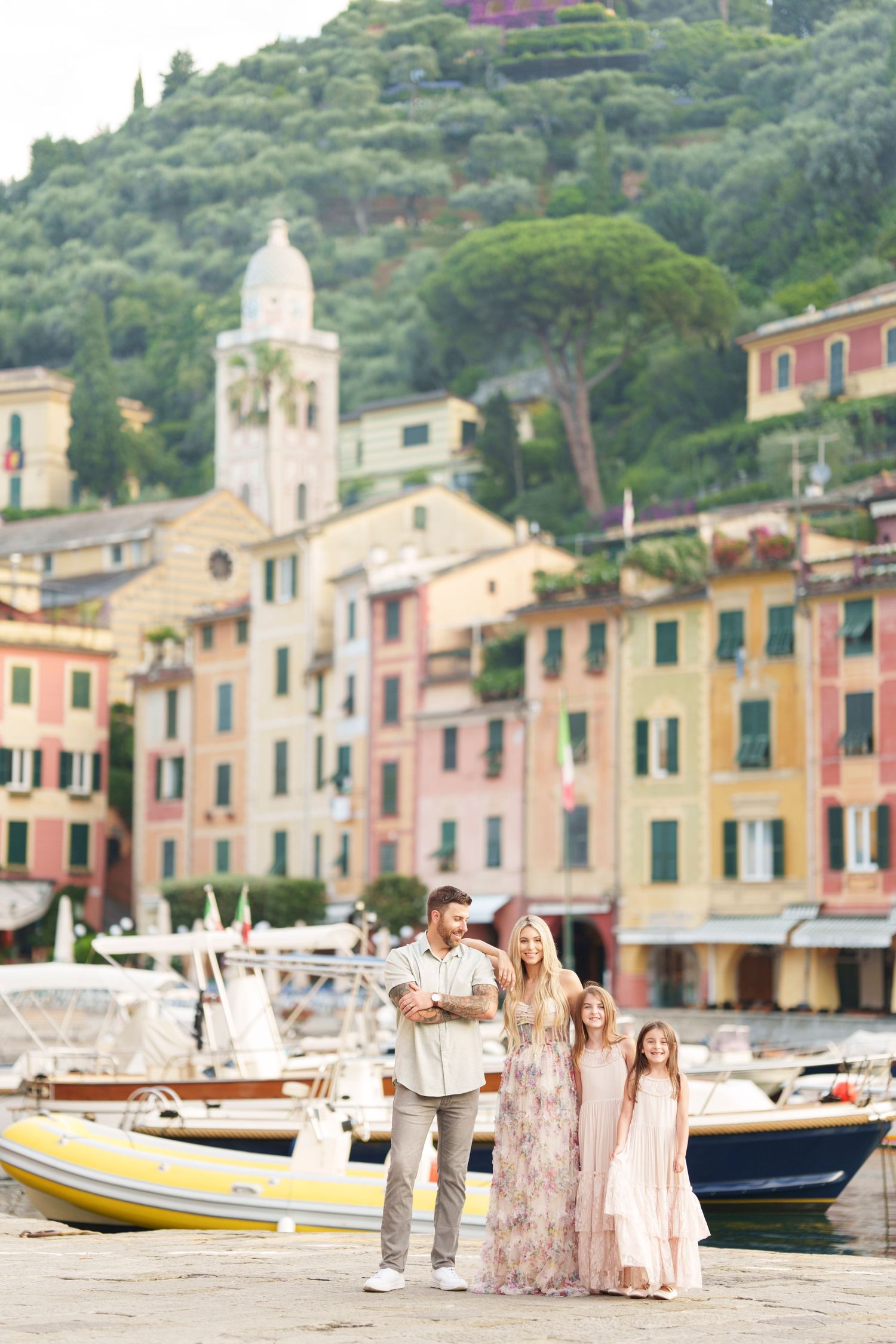 Family stands along colorful harbor of Portofino, Italy with pastel buildings and boats in background.