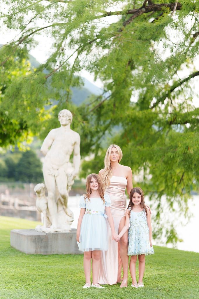 Family group poses together outdoors in coordinated pastel outfits under green trees in a park setting.