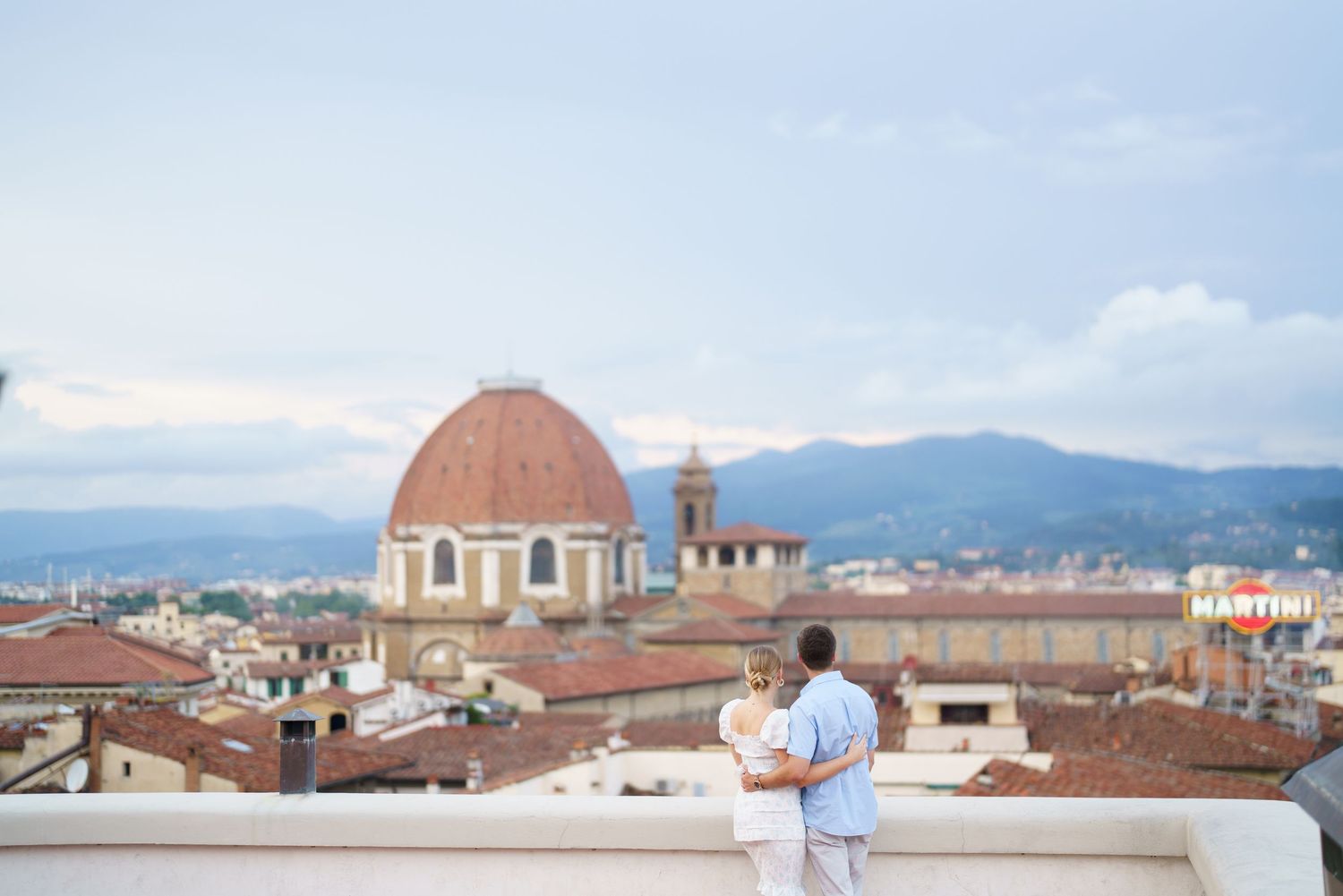 Panoramic view of Florence's historic skyline with terracotta rooftops and domed architecture against a blue sky.
